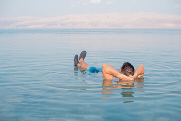 Man lies in blue water of Dead Sea. Very salty water push out. Treatment and recreation on beach, travel and holidays in Israel. Salt and mud healthy for body