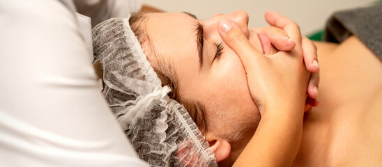 Face massage. Beautiful caucasian young white woman having a facial massage with closed eyes in a spa salon