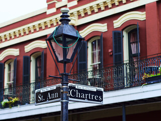 Closeup of a sign on a street lamp with the street names Chartres St. Ann against a red building.