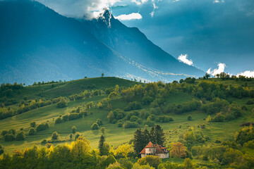Beautiful summer landscape with a small house in the green vale against the mountains.
