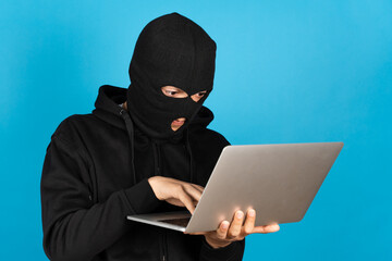 Hacker or online criminal typing on laptop isolated on blue background.