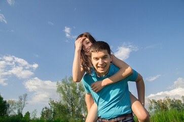 A young man carries his beautiful smiling woman on his back in the park. Couple in love having fun together.