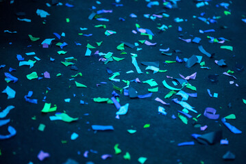 Thousands of confetti on the floor during a night festival. Image is ideal for backgrounds. Multicolor are the confetti in the photo. The floor as a background is black. Cold and blue tonality