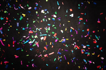 Thousands of confetti on the floor during a night festival. Image is ideal for backgrounds. Multicolor are the confetti in the photo. The floor as a background is black. 