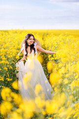young beautiful woman runs through a field with yellow flowers. The bride in a long white dress in a rapeseed field.
