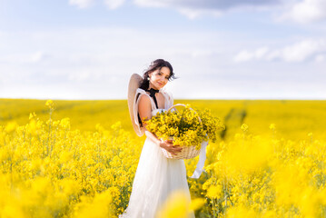 beautiful woman with a large basket of yellow flowers stands in a rapeseed field