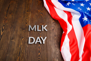 the word MLK day laid with silver metal letters on wooden surface with crumpled USA flag at upper...