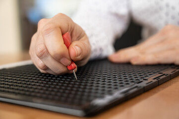 A woman uses a special stencil and stylus to write a letter in braille. 