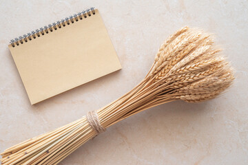 Blank notebook paper and bunch of wheat ears on marble background.
