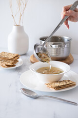 Table setting at home. Eating soup at dinner. Fresh vegetable soup with chicken broth. Healthy food concept. Minimalism in the interior of the kitchen. Chicken soup with vegetables in a white plate