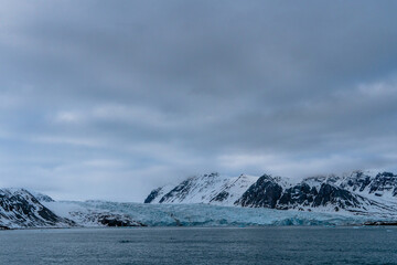 Melting glacier in Svalbard, Norway, with dark winter mountain with snow, sea.