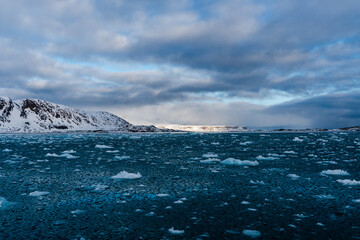 Fototapeta na wymiar Sea with melting ice cubes, snowy mountains In Svalbard, Norway. Global Warming.