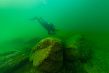 SCUBA diver exploring a cloudy inland lake and boulders with a diving torch