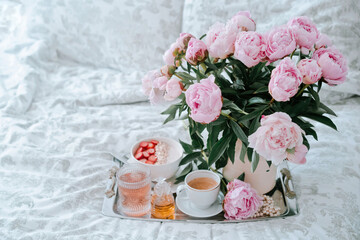 Tray with bouquet of pink peonies flowers and a cup of black coffee and Breakfast in bed, summer morning concept. Healthy food