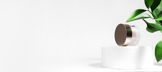 A mock up white jar of cream on a white gray background, on a white table with green leaves of a tropical plant, with hard shadows. Stylish look of the product, identity.
