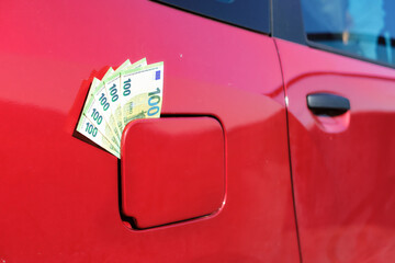 Close up of many hundred euro banknotes in the gas cap of a car. Symbolizes the rising price of...