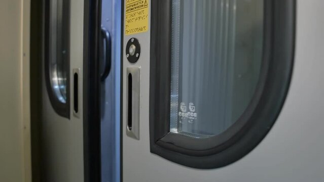 a woman's finger presses the button to open the train doors between the cars. The automatic door opens and the passenger goes to the next car