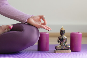 Woman practicing yoga, relaxing in Lotus pose on mat. Padmasana exercise close up, mudra hand and feet close up. Girl in purple sportswear, meditating in studio or at home Candles, Buddha figurine