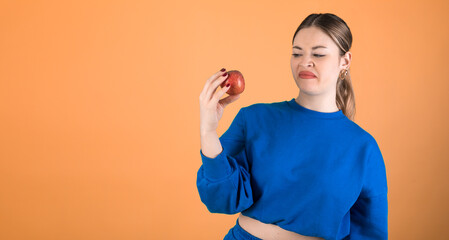 Woman rejecting an apple. Orange background. 20-22 years old woman. Caucasian woman.