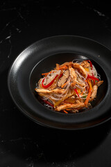 Funchoza with chicken and vegetables on a black background, top view, copy space. Glass noodles, Asian food.