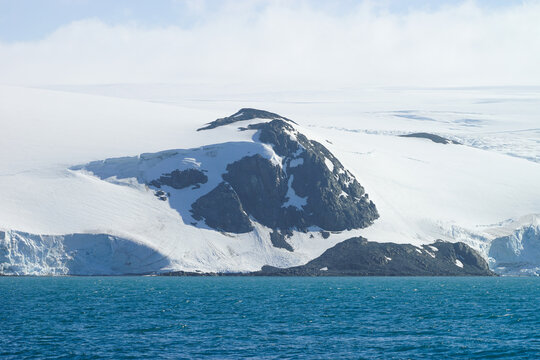 A huge Antarctica rock mountain and snow iceberg with blue sky and sea