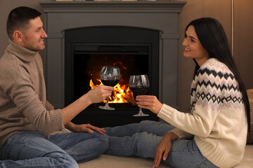 Lovely couple with glasses of wine spending time together on floor near fireplace at home
