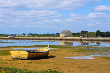 Vue lointaine d'une barque jaune et bleue posée sur le sable à la marée basse sur l'île d'Arz...