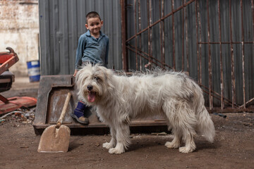 A child plays with a dog at dad in the garage. Children's activity on the street. A boy with his friend. A shaggy white dog guards a child. Active and naughty five year old baby.