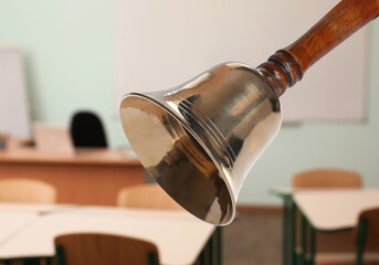 Golden school bell with wooden handle and blurred view of empty classroom