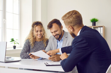 Happy young family at meeting in office signs document on purchase of real estate or loan agreement. Head of bank, realtor or financial advisor submits contract and indicates place of its signing.. - obrazy, fototapety, plakaty