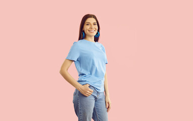 Studio shot of happy beautiful confident young woman wearing blue cotton T shirt, comfortable blue jeans, and pretty earrings standing isolated on light pink colour background. Casual fashion concept