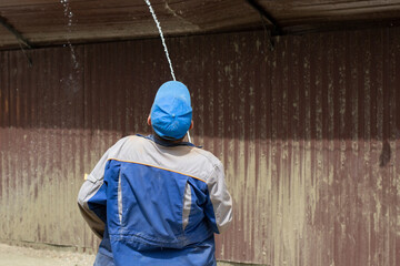 A man washes the fence with a hose. The builder cleans the fence from dirt.