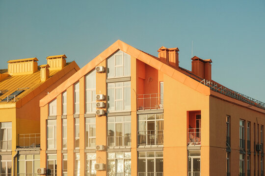Sharp house roof of orange or yellow modern residential building with many windows in golden hour at sunset beautiful sun rays on the facade of a building in the capital of Ukraine Kiev. Retro