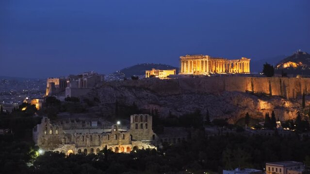 Famous greek tourist landmark - the iconic Parthenon Temple at the Acropolis of Athens as seen from Philopappos Hill in the evening blue hour, Athens, Greece. Horizontal camera pan