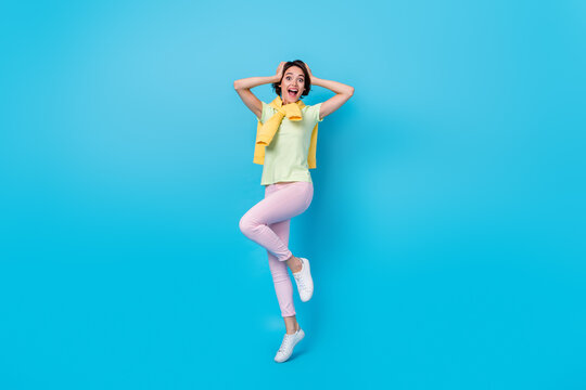Full body photo of cool young brunette lady jump look camera wear t-shirt pants sneakers isolated on blue background