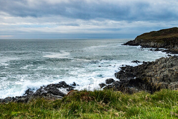 From a green headland, looking across a rocky cove on a cold November day, with a dramatic sky.