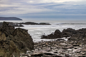 Stones and rocks on the beach, with the sea and a dark headland beyond.