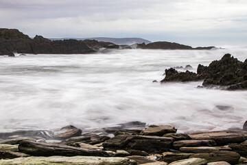 Large pebbles in the foreground and dramatic rocks rising rom the sea, with a dark headland in the...