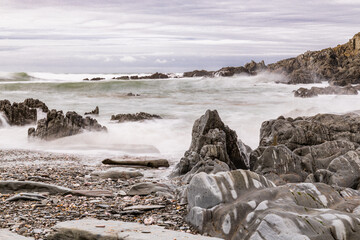 A rocky and pebbly beach in North Devon, with the sea crashing onto the beach.  A big wave is approaching in the distance.