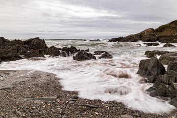 A waves laps on the beach as a the next one approaches in the background.  The rocks and pebbles on the beach are beautifully atmospheric.