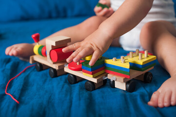 Toddler boy plays with wooden constructor train on bed close-up.