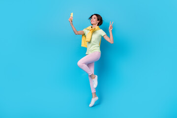 Fototapeta na wymiar Full length photo of cute millennial brunette lady jump do selfie wear t-shirt pants shoes isolated on blue background