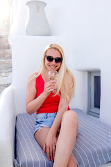 beautiful blonde woman in sunglasses sitting on sofa and drinking wine