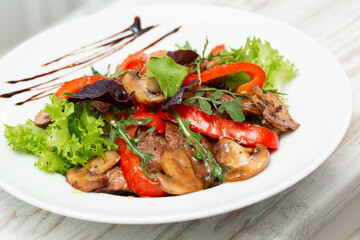 Veal salad with lettuce, red pepper and mushroom on white plate on wooden background, copy space. Restaurant food, close up. Meat salad