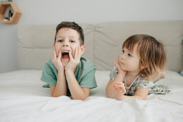 Older brother and younger sister playing in the bedroom on the bed