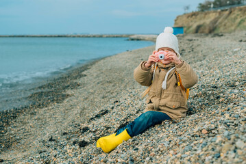 a little girl squinting photographs the autumn seascape on a childrens pink camera. the child is passionately engaged in his hobby: photography