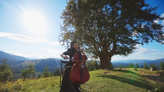 Middle-aged woman with makeup and nice black dress performs cello music. Lady closed her eyes enjoying music.