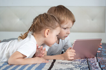 Kids and gadgets. A boy and a girl are lying on the bed and looking at a tablet