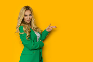 Blond woman in green jacket is pointing with two fingers.