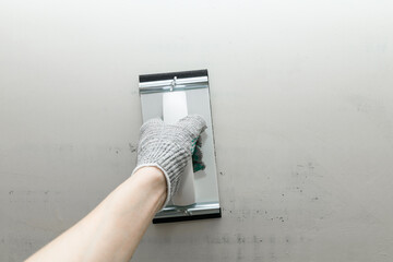 Plaster float in male hand in glove against a gray wall. Plastering grater in the hands of a worker...
